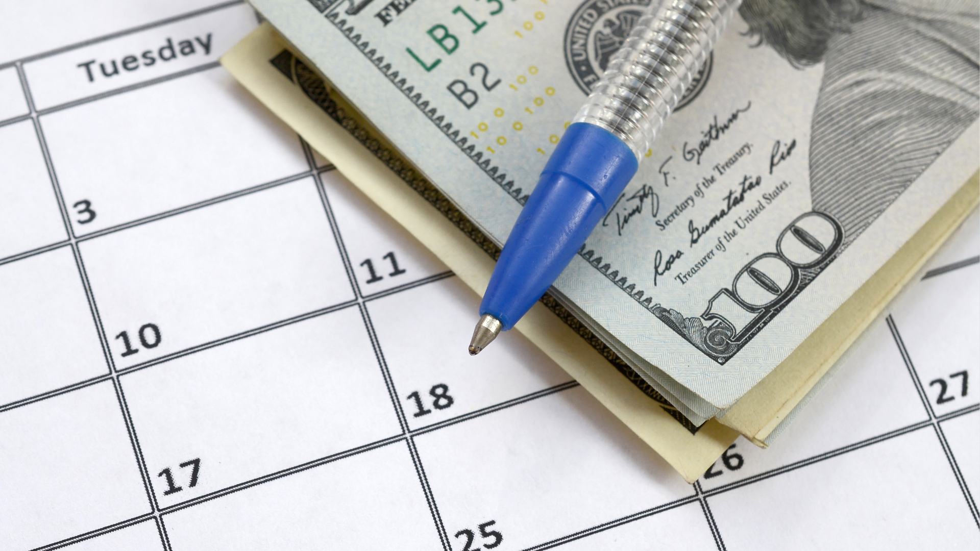 A close-up of a calendar with a stack of $100 bills and a blue pen resting on top, symbolizing the importance of Annual Budget Planning Services in organizing financial resources and preparing for a successful business year.