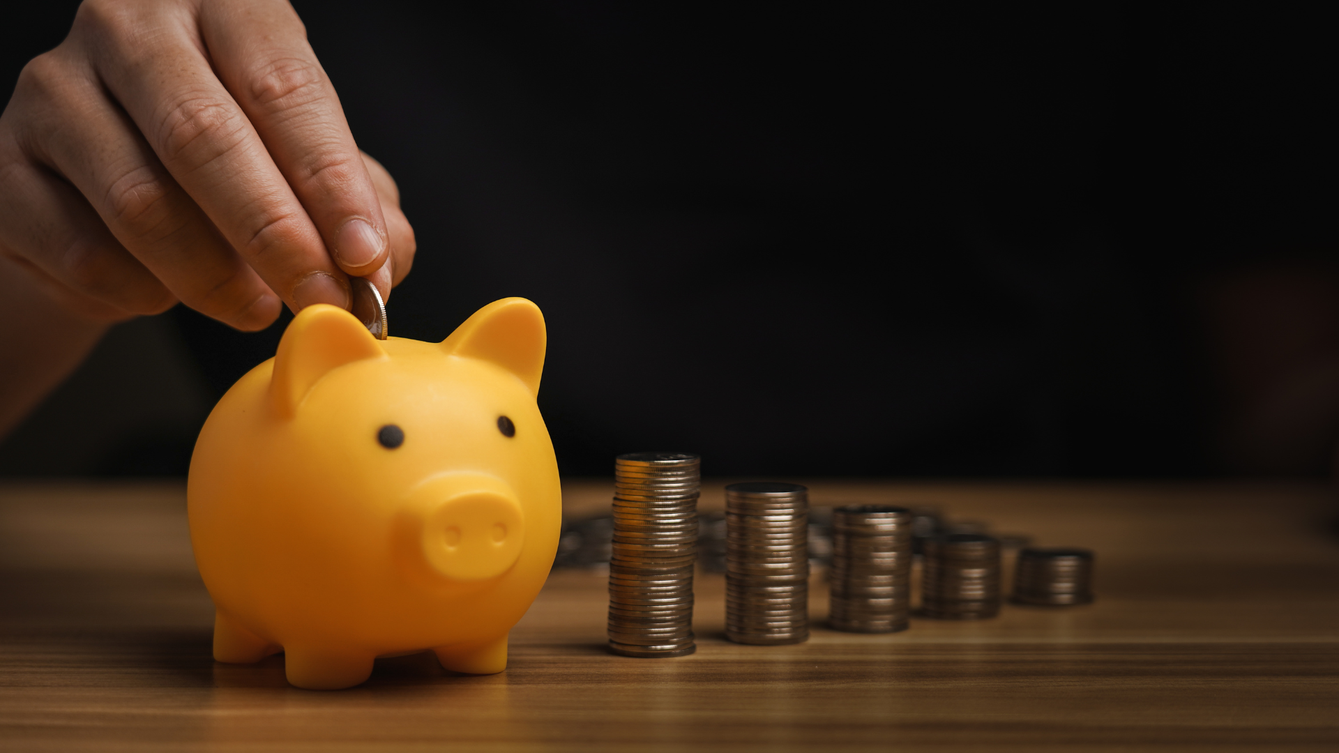 Hand placing a coin into a yellow piggy bank with stacked coins in the background, symbolizing cash reserve planning services for building a financial safety net for businesses.